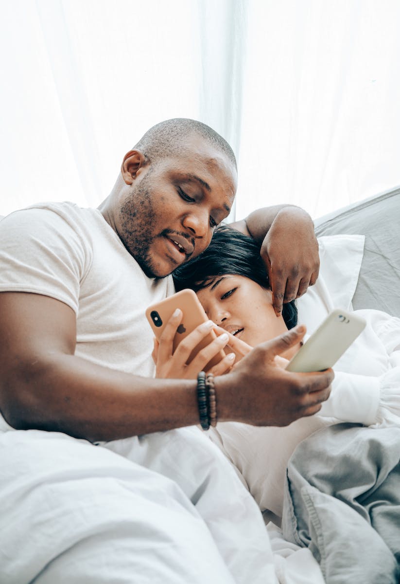 Cheerful young spouses messaging on smartphones in bed